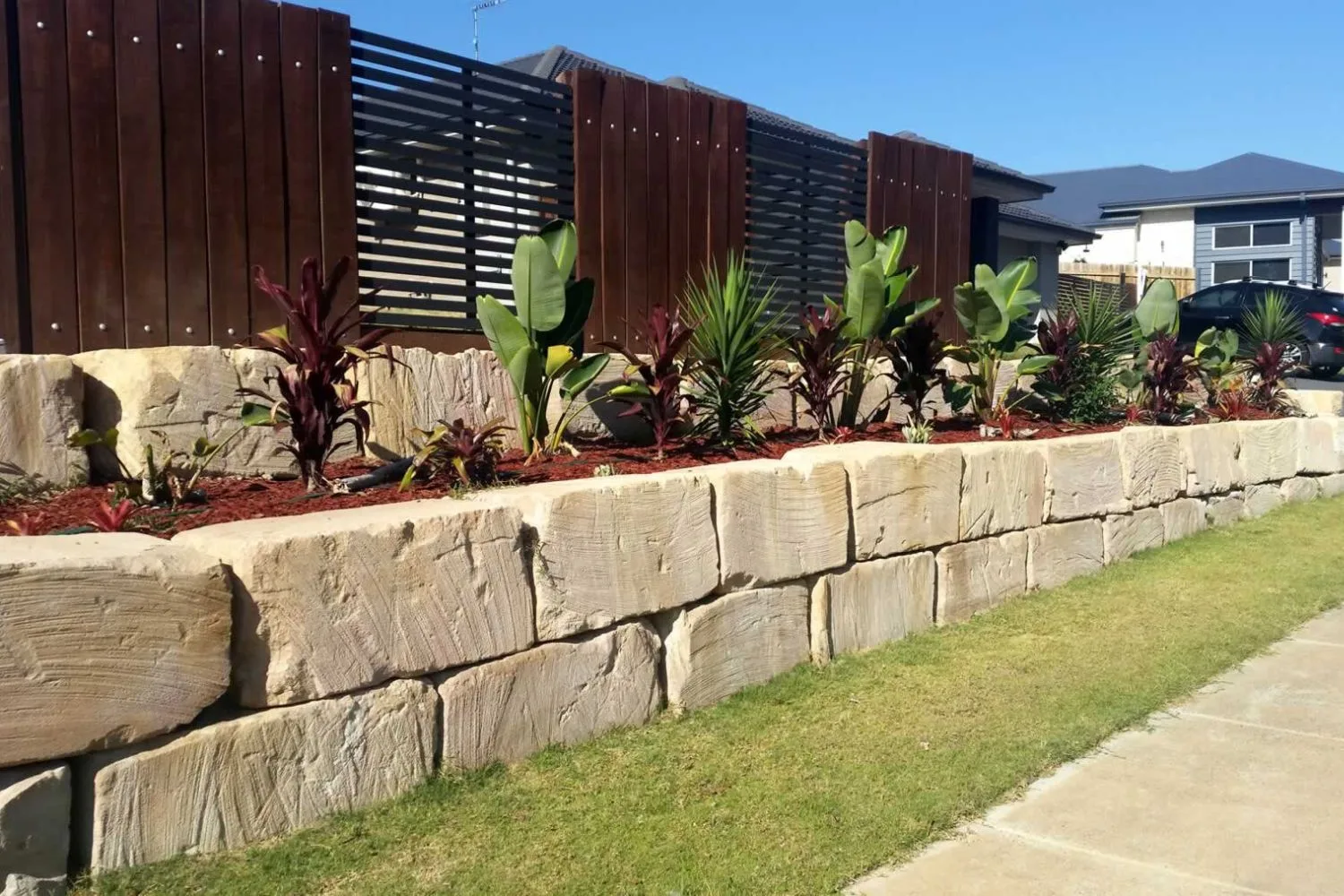 Sandstone block retaining wall and steps lit at dusk in front of a modern home