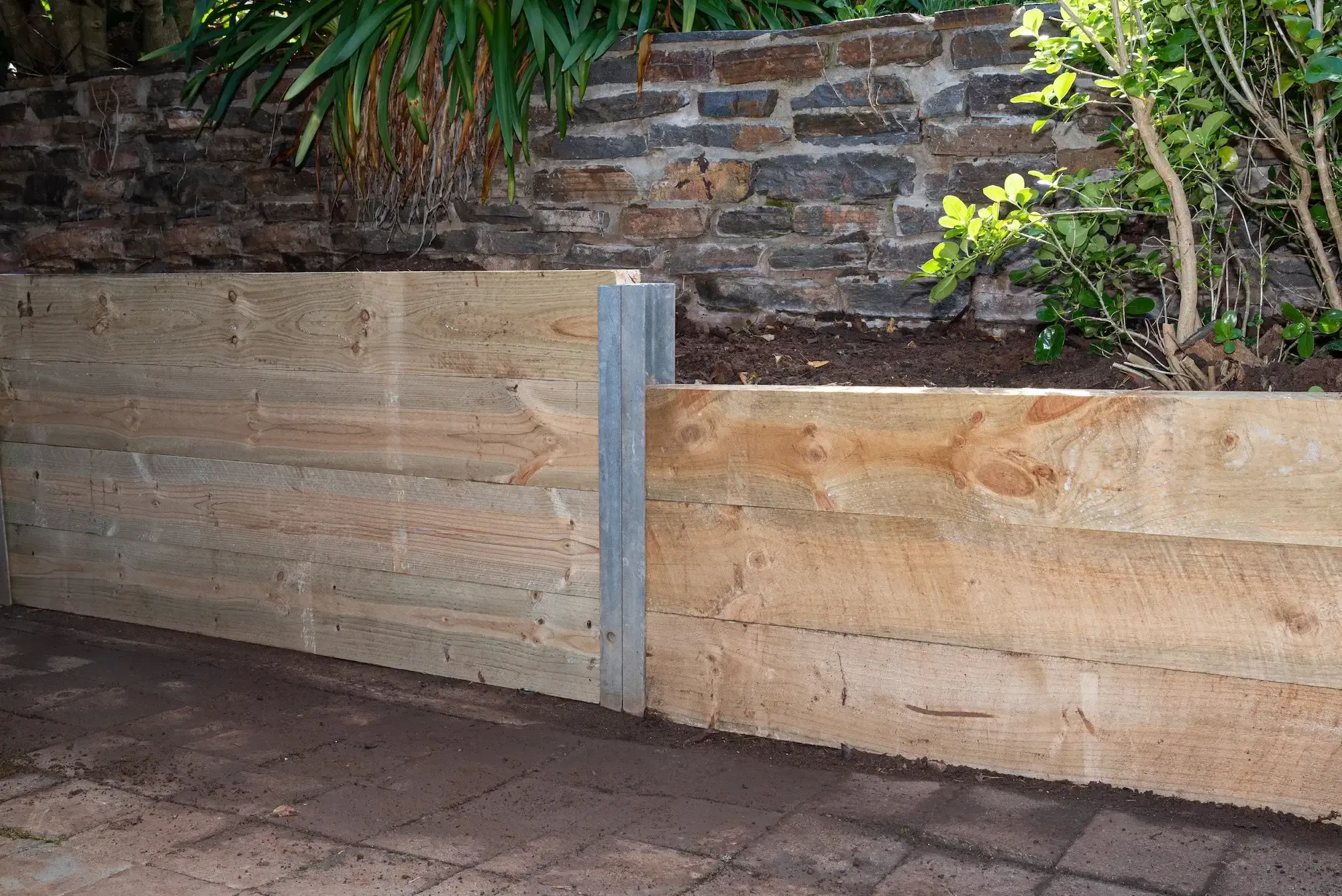 Timber retaining wall at dusk beside an old stone wall